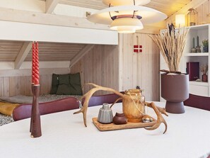 A cozy room with a sloped ceiling, a wooden bed with green pillows, a red candle, a wooden chair, a tray with a teapot, and a vase with dried plants. - 4 Star Holiday Home in Hjorring (Hjørring)