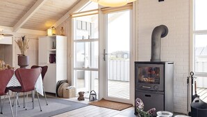 A cozy living room with a fireplace, a dining area with red chairs, and a view through a glass door.