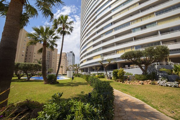 A modern hotel with multiple floors, a swimming pool, and well-maintained gardens.