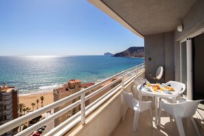 A balcony with a table set for breakfast overlooking a beach and the sea.