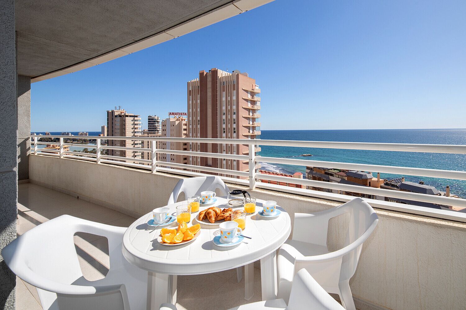 A balcony with a table set for breakfast, overlooking a beach and cityscape.