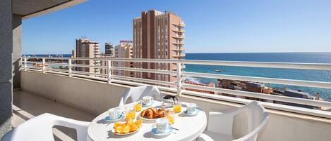 A balcony with a table set for breakfast, overlooking a beach and cityscape.