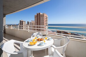 A balcony with a table set for breakfast, overlooking a beach and cityscape.