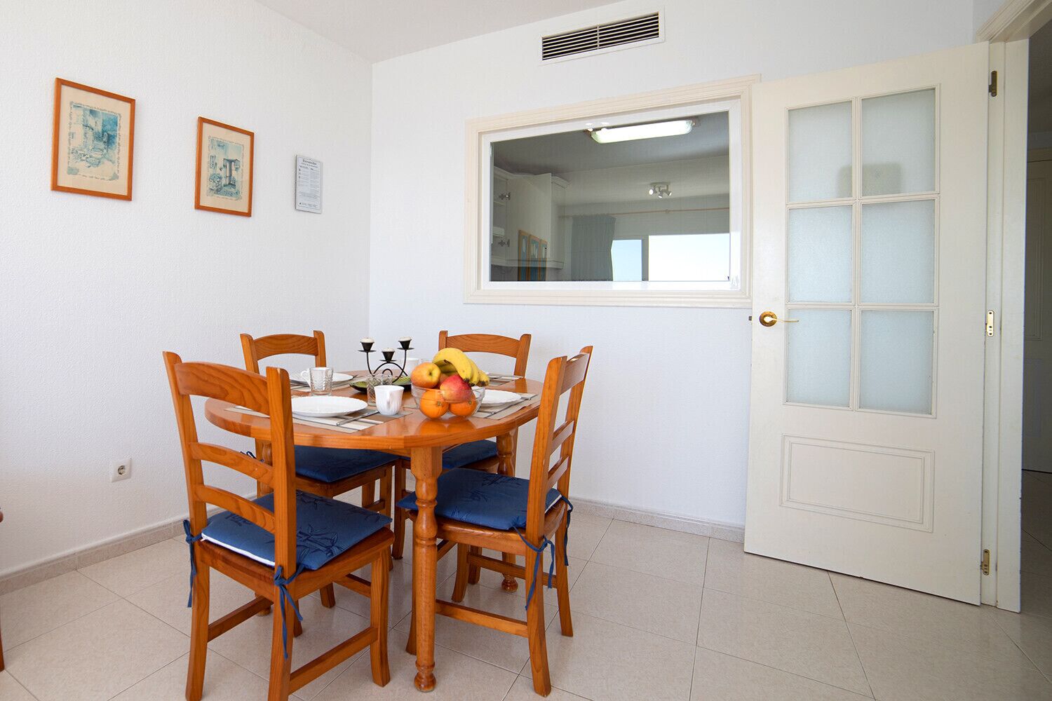A dining area with a round wooden table, six chairs, and a fruit bowl.