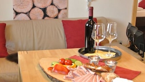Una mesa de madera con una tabla de fiambres, una botella de vino, copas y un vaso de cerveza.