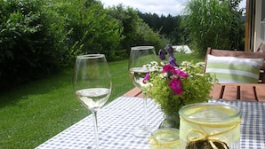 Mesa al aire libre con mantel a cuadros, dos copas de vino, un florero con flores y dos frascos con hierbas.