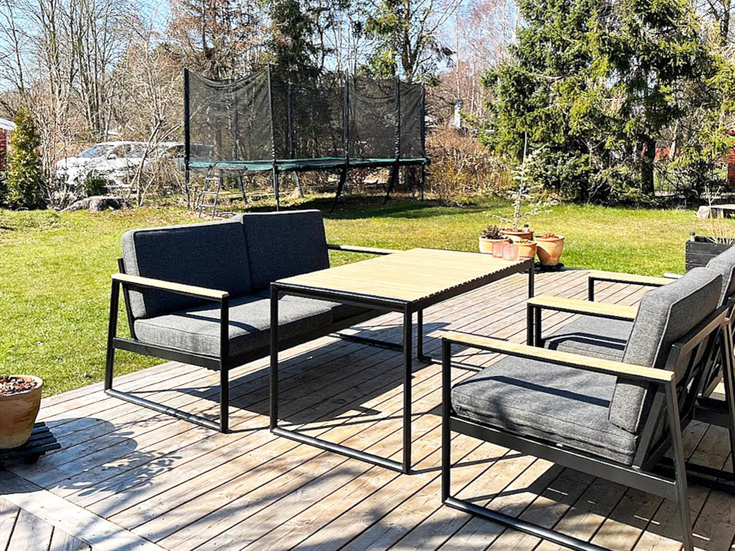 An outdoor deck with a wooden table and two chairs, surrounded by a grassy area and trees.