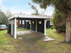 Un bâtiment d’un seul étage avec un porche couvert, un véhicule garé à l’extérieur et un arbre sur la droite.