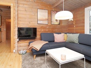 A cozy log cabin interior with a dark blue sofa, a white coffee table, and a mounted flat-screen TV. - 7 Person Holiday Home in Hojby (Hojby)