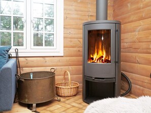 A wood-burning stove in a log cabin with a view of trees outside. - 7 Person Holiday Home in Hojby (Hojby)