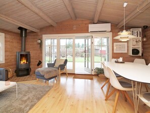 A cozy room with a wood-burning stove, a dining area with a white table and chairs, and a large sliding glass door leading to an outdoor area. - 7 Person Holiday Home in Hojby (Hojby)