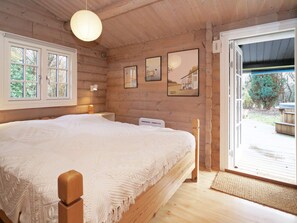 A wooden cabin bedroom with a large bed, a wooden headboard, a hanging light fixture, and a door leading to a deck. - 7 Person Holiday Home in Hojby (Hojby)