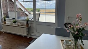 Une pièce dotée d’une grande fenêtre, d’un radiateur blanc, d’une table ornée d’un vase de fleurs et offrant une vue sur l’extérieur.