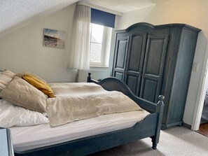A bedroom with a bed, a wardrobe, a window with curtains, and a radiator. - Fehmarn Room With Lake View (Fehmarn)