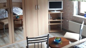 Habitación tipo dormitorio con una cama, un escritorio, una silla, un armario, un televisor y una ventana con cortinas.