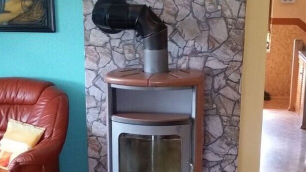 Una habitación de esquina con pared de piedra, un sofá de cuero rojo y una estufa de leña.