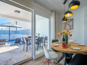Uma área de refeições com uma mesa posta para quatro pessoas, um vaso de flores e vista para a piscina.