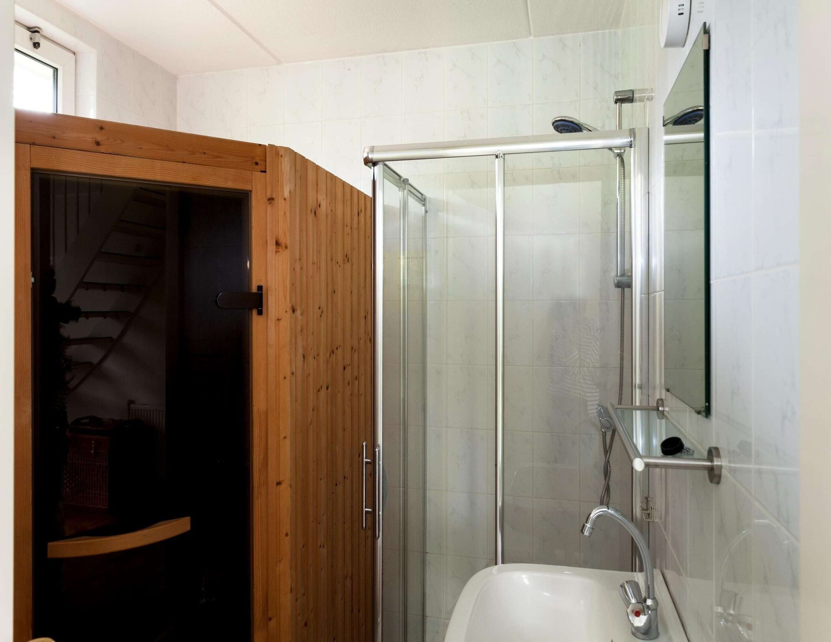 A bathroom with a wooden door, a glass shower enclosure, a sink, and a mirror.