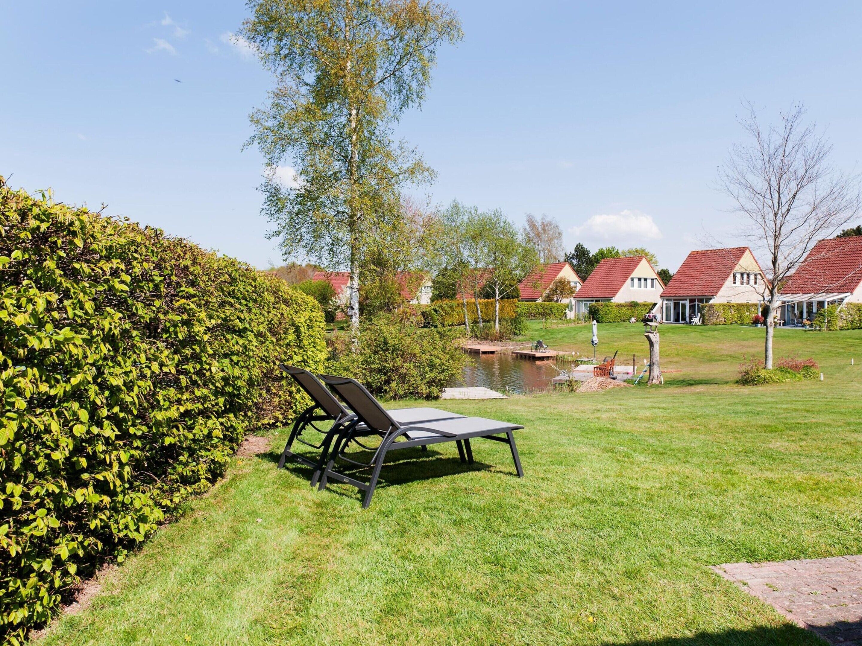 A well-maintained garden with a pond, a lounge chair, and a row of houses with red roofs.