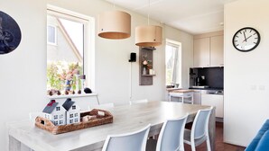 A modern kitchen with a built-in oven, a dining area with a wooden table and white chairs, and a blue sofa. - Holiday Home in Groningen With Pool (Vlagtwedde)