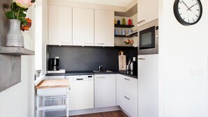 A modern kitchen with white cabinets, a black countertop, a microwave, and a clock on the wall. - Holiday Home in Groningen With Pool (Vlagtwedde)