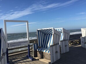 A beachside seating area with striped blue and white chairs and a wooden deck. - Schatz Comfortable Holiday Residence (Wenningstedt-Braderup)