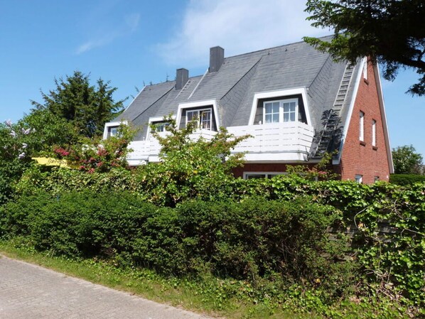 A two-story house with a sloped roof, white exterior walls, and a brick chimney. - Schatz Comfortable Holiday Residence (Wenningstedt-Braderup)