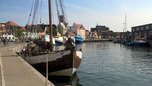 Um porto com barcos atracados, uma passarela para pedestres e edifícios ao fundo.