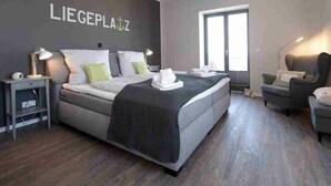 Quarto moderno com uma cama grande, mesas de cabeceira, uma cadeira e uma janela.
