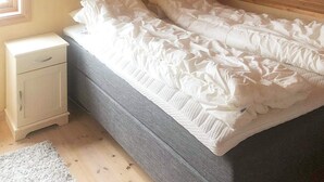 Una cama individual con ropa de cama blanca en una habitación con paredes de madera y una mesita de noche pequeña.