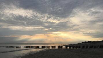 A beach with a wooden pier extending into the water, under a cloudy sky.