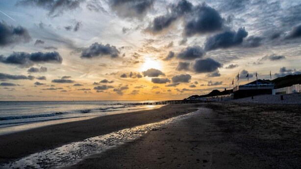 Ein Strand mit einem Steg, der sich ins Wasser erstreckt, bewölkter Himmel und Sonnenuntergang.