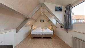 Ein Schlafzimmer mit schrägem Dach, zwei Betten, Nachttischlampen, einem fenster mit Vorhängen und einer Heizung.
