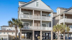 A multi-story residential building with a balcony on the second floor, a garage, and a stone facade. - 6BR North Myrtle Beach House with private pool and loads of fun (North Myrtle Beach)