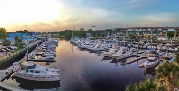 A marina with numerous boats docked, a bridge in the background, and a calm water body.