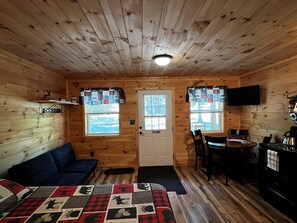 A cabin interior with a bed, a sofa, a dining table with chairs, a television, and a fireplace. - Cabin 1
Recreational Cozy Cabin Rentals (Sangerville)