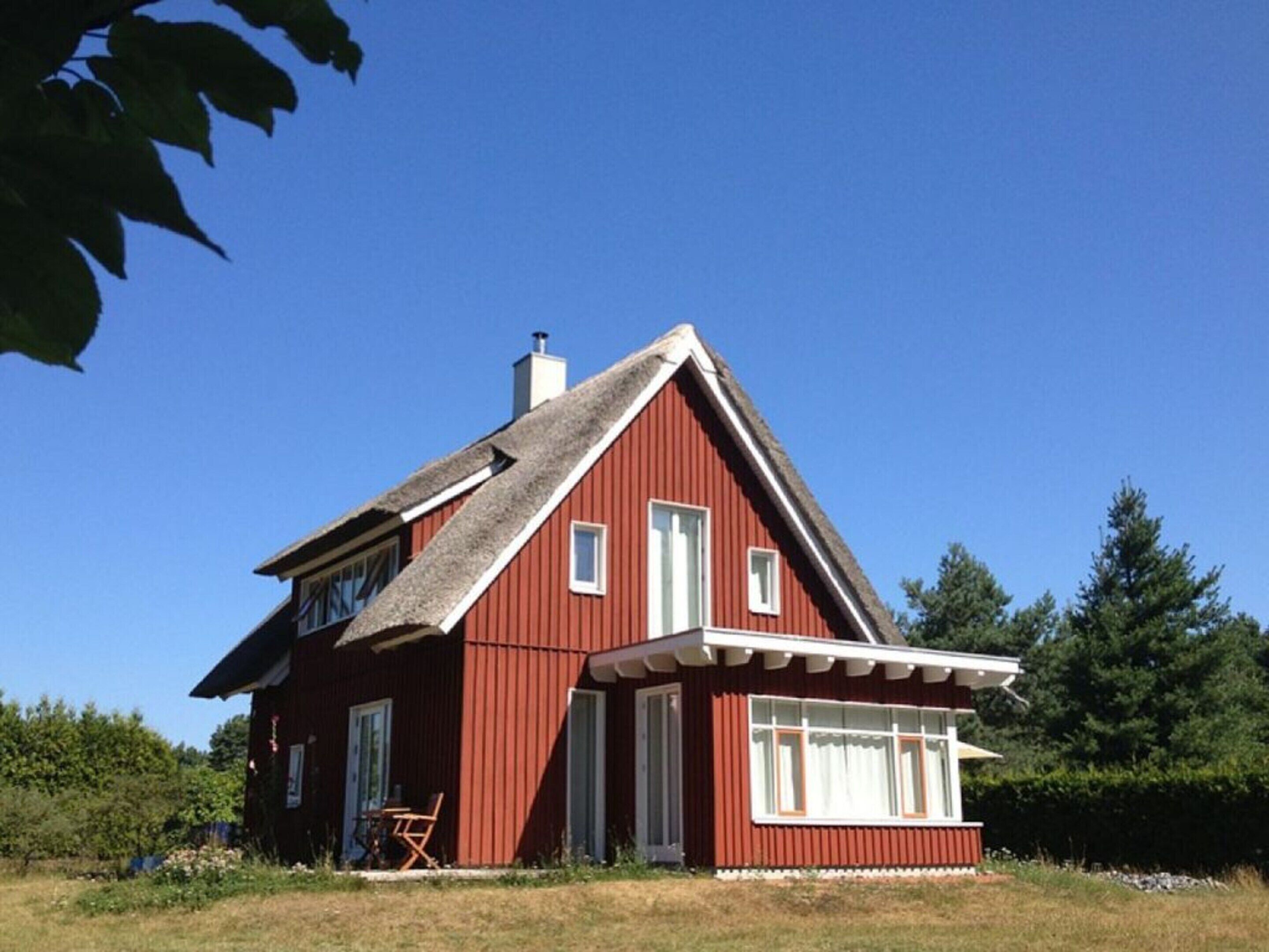 Ein rotes Holzhaus mit geneigtem Dach, Schornstein und einer kleinen Veranda mit Tisch und Stühlen.