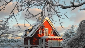A red wooden house with a sloped roof, surrounded by snow-covered trees and a clear sky. - Holiday Apartment Haus Sundevit (Pruchten)