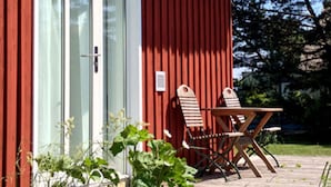 A red building with a glass door, a small table, and two wooden chairs outside. - Holiday Apartment Haus Sundevit (Pruchten)