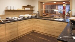A modern kitchen with wooden cabinets, a black countertop, and various food items.