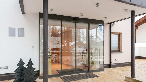 A modern building entrance with a glass door, a metal sculpture, and a paved area.