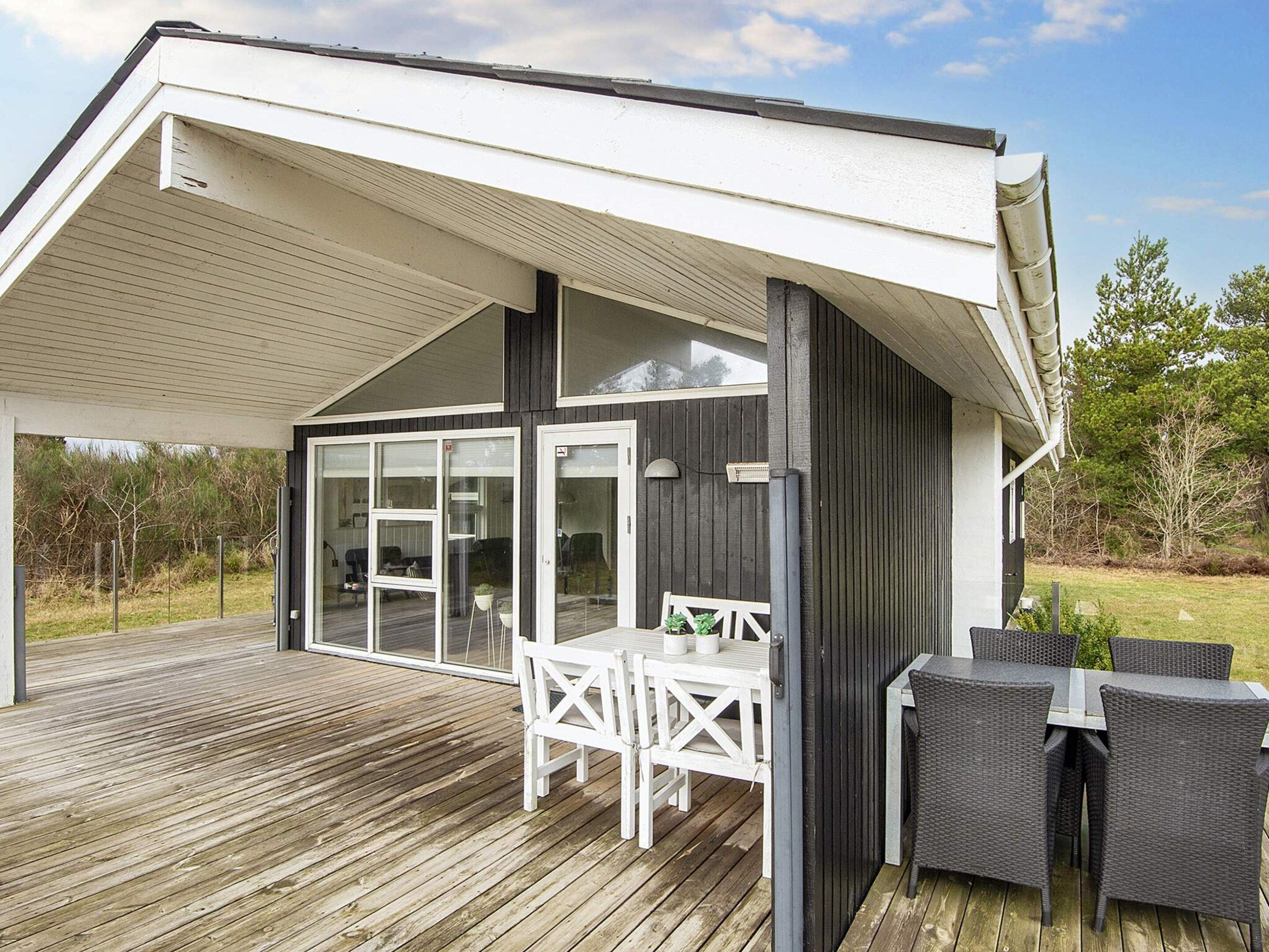 A covered outdoor deck with a table and chairs, a glass door entrance, and a view of the surrounding landscape.