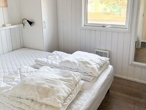 Una cama individual con ropa de cama blanca en una habitación con paredes de madera y una ventana.