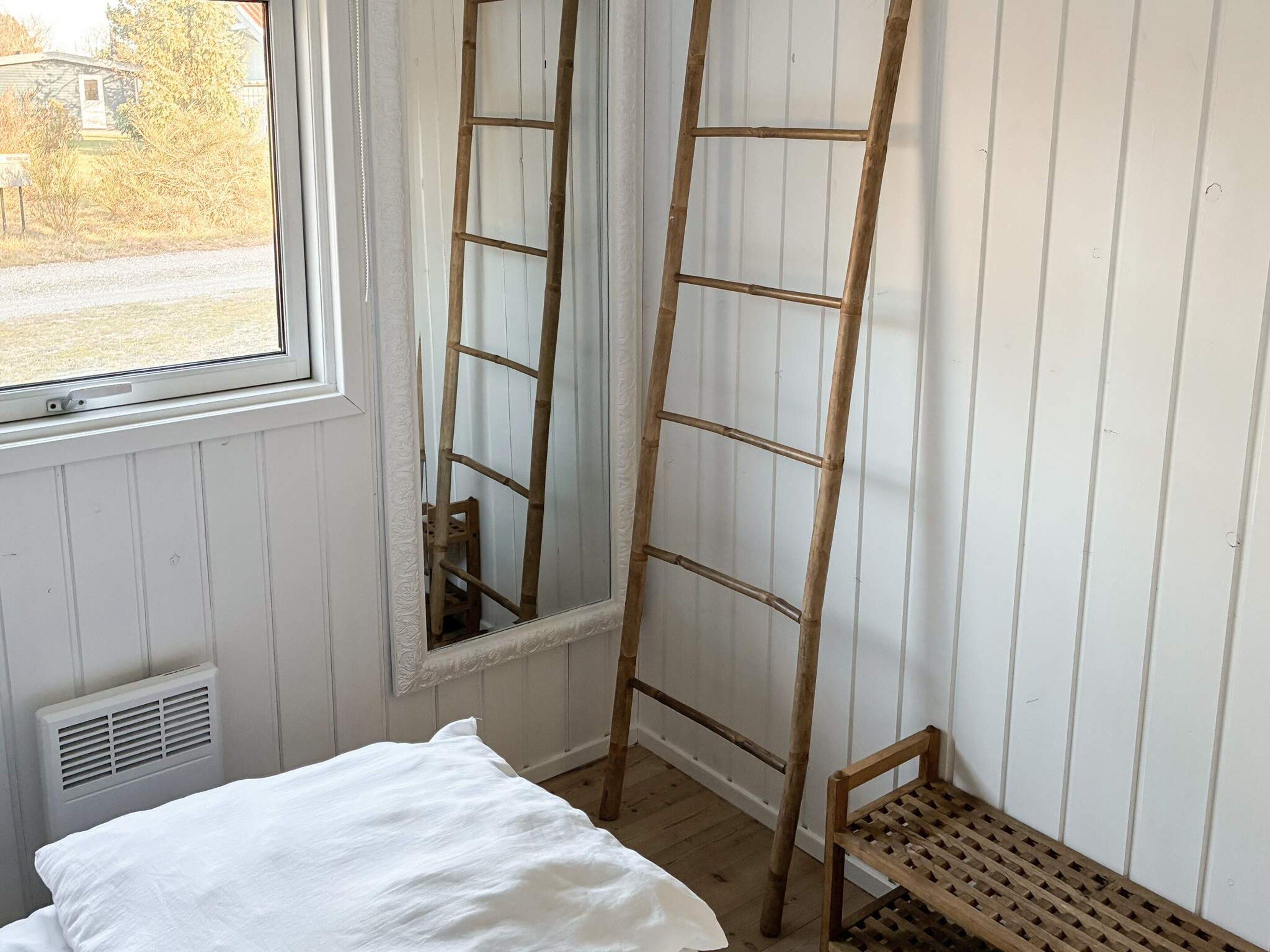 Une pièce avec un lit, une fenêtre, une échelle en bois et un banc.