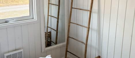 A room with a bed, a window, a wooden ladder, and a bench.