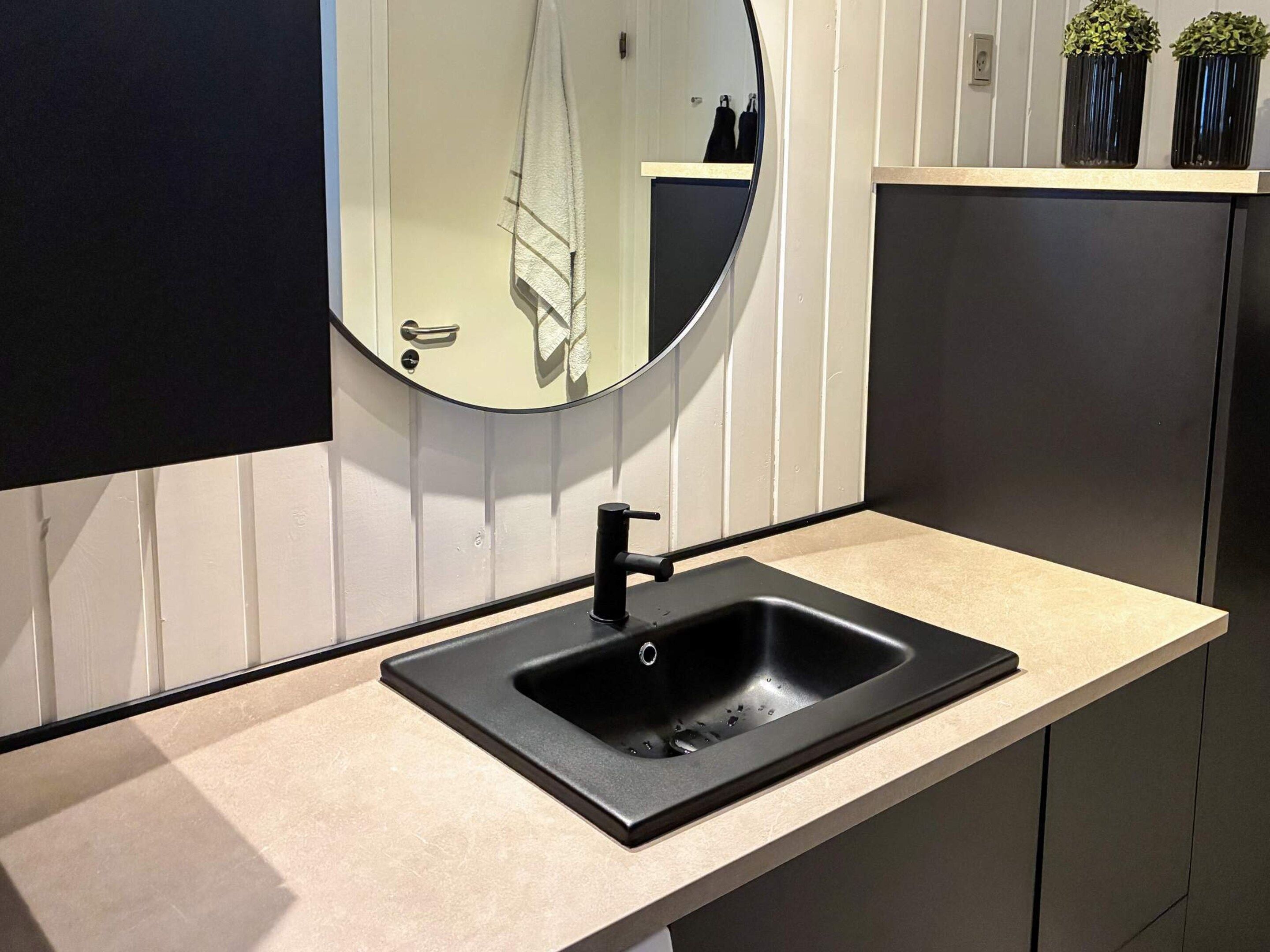 A modern bathroom with a round mirror, black sink, and a beige countertop.