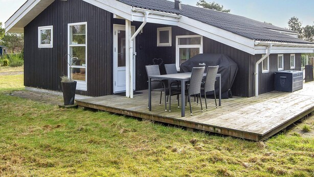 A modern outdoor patio with a table and chairs, a barbecue grill, and a wooden deck. - 4 Star Holiday Home in Juelsminde (Juelsminde)