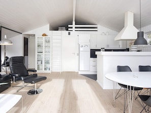 A modern kitchen with white cabinetry, a central island, and a dining area with a round table and chairs. - 4 Star Holiday Home in Juelsminde (Juelsminde)