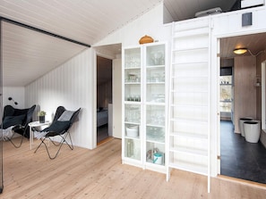 A room with a high ceiling, a wooden floor, a seating area with chairs and a table, and a large open shelving unit with glassware. - 4 Star Holiday Home in Juelsminde (Juelsminde)