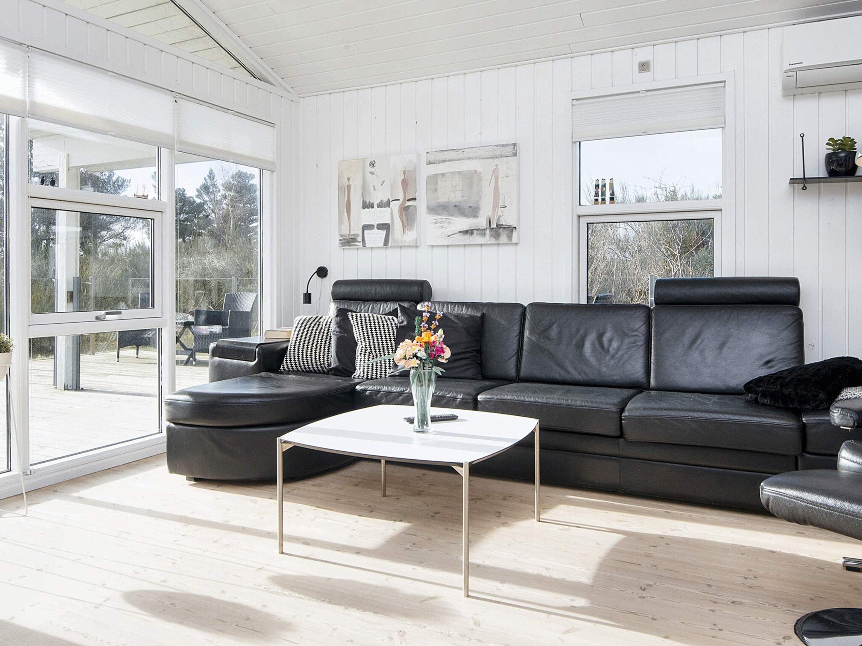 Una sala moderna con un sofá de cuero negro, una mesa de centro blanca y un ventanal que ofrece vistas al exterior.